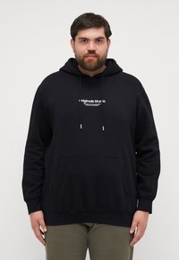 Svart hettegenser med lommesekk foran og hvit trykket logo. Har snor og ribbestrikkede cuffs ved ermer og hem.
