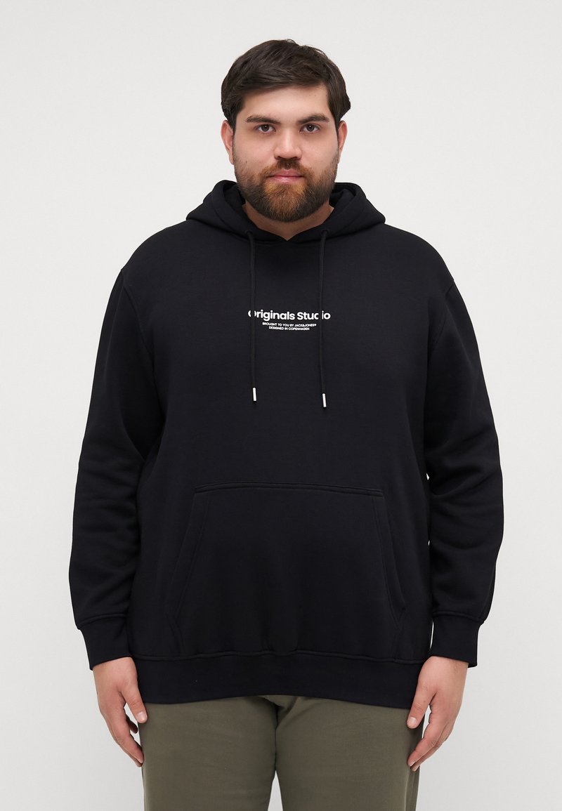 Svart hettegenser med lommesekk foran og hvit trykket logo. Har snor og ribbestrikkede cuffs ved ermer og hem.