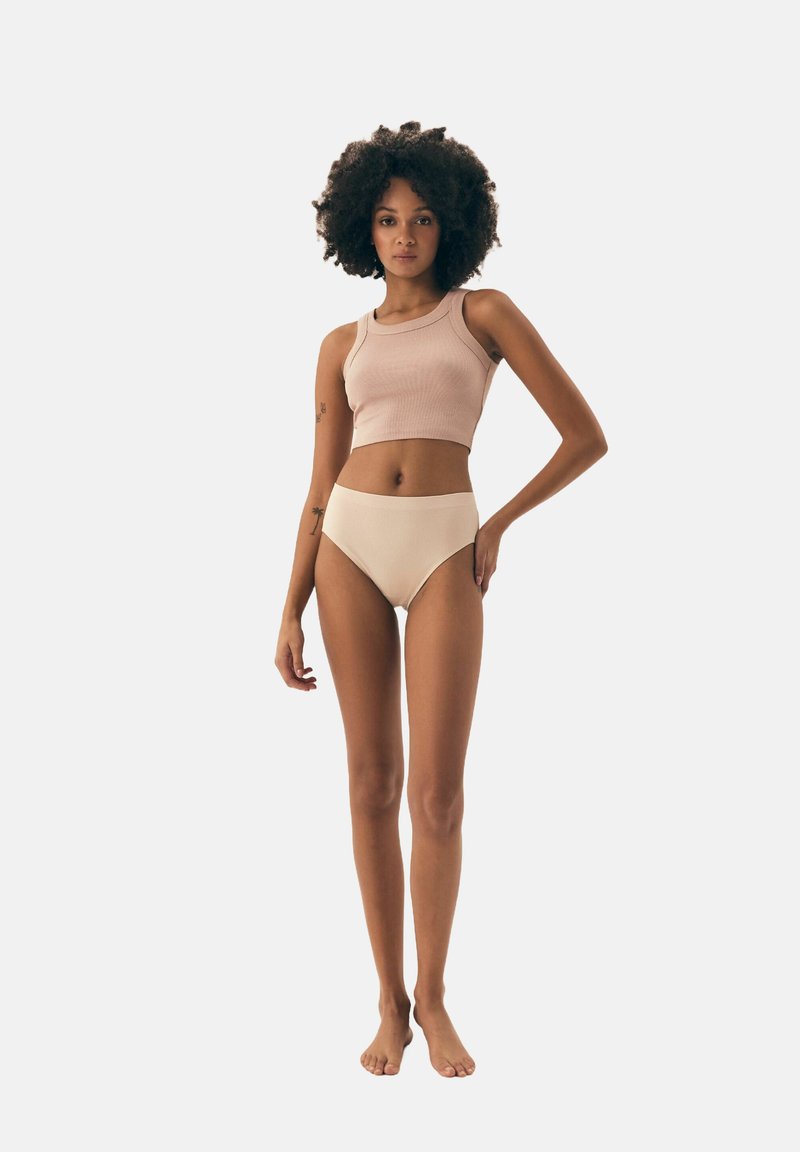 Wyprofilowany, prążkowany różowy top crop oraz beżowa bielizna z wysokim stanem, wykonane z miękkiego materiału, o gładkiej teksturze i dopasowanym kroju, prezentowane na modelce.