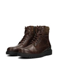 Un par de botas de cuero marrón con cordones, con cuellos acolchados y suelas de goma negra, inclinadas ligeramente hacia la derecha sobre un fondo blanco.
