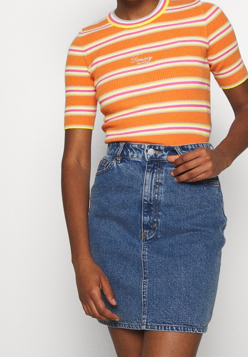 Camiseta naranja de canalé con rayas rosas y blancas, combinada con una falda de mezclilla azul de cintura alta. Tiene un cuello redondo y cierre de botones en la parte frontal.