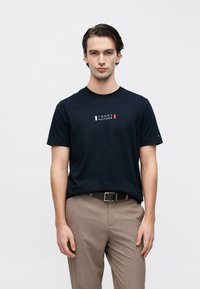 Μπλε σκούρο βαμβακερό μπλουζάκι με στρογγυλή λαιμόκοψη και κοντά μανίκια, με σχέδιο λογότυπου σε λευκό, κόκκινο και μπλε στο στήθος.