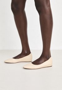 Beige, flat ballerina shoes made of smooth material, featuring a pointed toe and a low heel, with a minimalistic design.