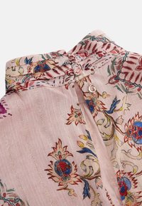 Blomstermønstret stoftop i blød pink, med dekorativ syning, en knapløbning og et lille metallogo-udsmykning.