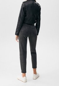 Chaqueta de cuero negra cropped combinada con unos vaqueros de cintura alta en gris oscuro. Zapatillas blancas completan el conjunto. Enfócate en la forma y el ajuste.