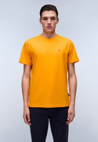 Bright orange short-sleeve t-shirt made of cotton with a round neckline and a small brand logo on the chest. Worn with dark pants.