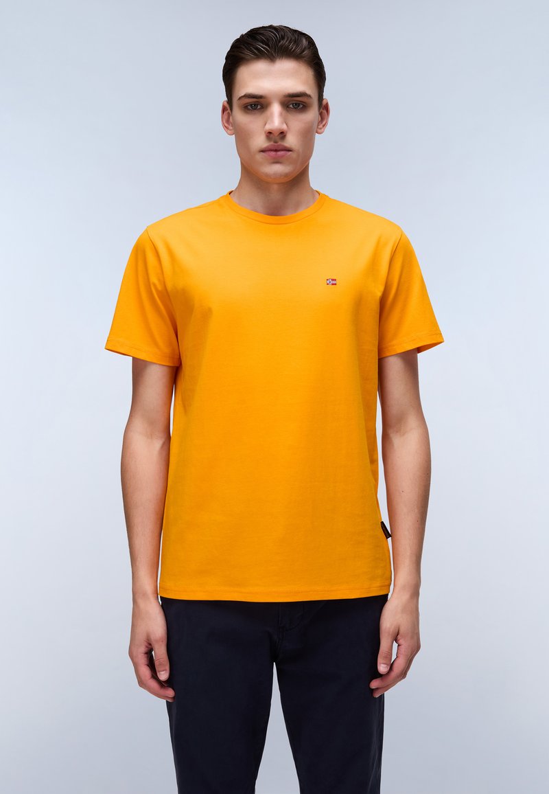 Bright orange short-sleeve t-shirt made of cotton with a round neckline and a small brand logo on the chest. Worn with dark pants.