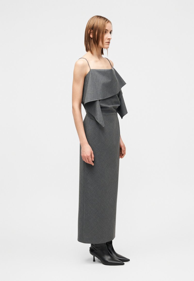 Robe grise avec détail de volants superposés au niveau de l'encolure, coupe ajustée et jupe longue jusqu'au sol. Comprend de fines bretelles et une texture de tissu.