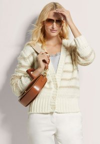 Crème en beige gestreepte gebreide cardigan met ribbels aan de onderkant, gecombineerd met een lichtgrijze top en een bruine leren tas, verfraaid met oversized zonnebrillen.