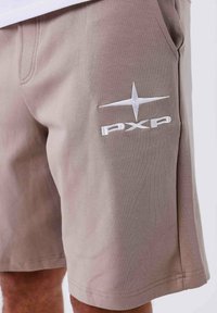 Lichtbruine shorts van zachte stof, met een wit geborduurd logo "PXP" en een sterontwerp op de linker bovenbeen.