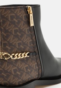 Bottine en cuir noir avec motif monogramme marron, ornée d'une chaîne dorée et d'un tire-zippe estampillé sur le côté.