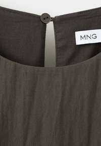 Gros plan d'un col de vêtement en tissu foncé avec une fermeture par boucle et bouton et une étiquette blanche affichant la marque "MNG".