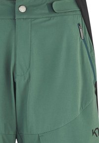Shorts d'extérieur verts en tissu léger, dotés d'une poche zippée, d'un devant plat et d'une fermeture à bouton-pression, avec un design incurvé au niveau de l'ourlet.