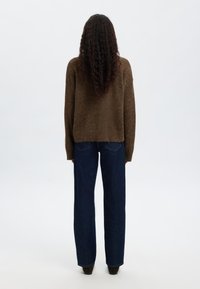 Barna kötött pulóver laza szabással, sötétkék egyenes szárú farmerral párosítva. A pulóver puha tapintású és bordázott mandzsettákkal rendelkezik.