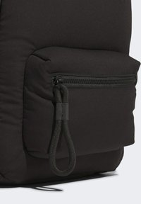 Detailní záběr na černou vycpanou tkaninu s obdélníkovou zipovou kapsou, která má na pravé straně silný smyčkový zip.