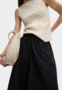 Beige räfflad topp med guldprickar, kombinerad med en svart kjol med elasticitet i midjan. Håller en krämfärgad vadderad handväska med veckad struktur.
