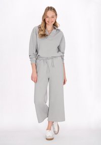 Jumpsuit grigio in maglia con colletto, vita elastica e gambe ampie. Presenta un motivo testurizzato, abbinato a sneaker bianche.
