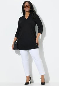 Schwarzes V-Ausschnitt-Tunika mit Dreiviertelärmeln, kombiniert mit weißen Slim-Fit-Hosen, schwarzen High Heels und einer schwarzen Handtasche.