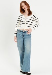 Cárdigan recortado a rayas blancas y negras con detalle de lazo, combinado con jeans de pierna ancha de color azul claro y botas negras. Conjunto simple y casual.