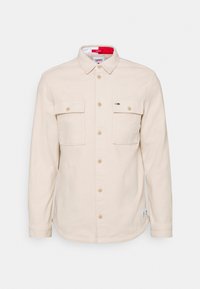 Camicia beige a maniche lunghe con bottoni, due tasche sul petto, colletto e un piccolo logo Tommy Hilfiger sulla tasca destra.