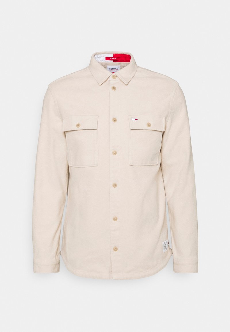 Camicia beige a maniche lunghe con bottoni, due tasche sul petto, colletto e un piccolo logo Tommy Hilfiger sulla tasca destra.