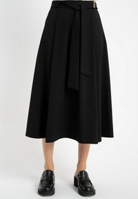 Czarna spódnica do kolan w zwiewnym fasonie z paskiem w talii i bocznymi wiązaniami. Gładki materiał z delikatnym połyskiem. Noszona z czarnymi mokasynami.