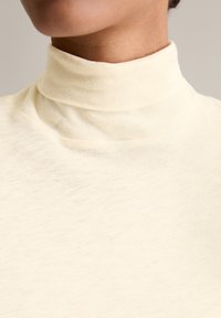 Cream turtleneck top with a soft, textured fabric. High collar design and seamless neckline create a smooth silhouette.