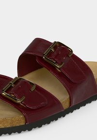 Sandale marron avec deux brides réglables comprenant des boucles dorées, semelle intérieure en liège et semelle extérieure noire texturée.