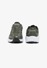 Sneakers verdi con tomaia testurizzata, chiusura con lacci e suola bianca. Il retro presenta un logo Lacoste e fori per la traspirabilità.
