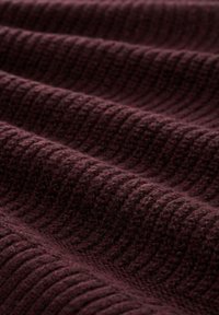 Tissu tricoté bordeaux foncé avec un motif en côtes et une texture douce et surélevée, présenté en détail rapproché.