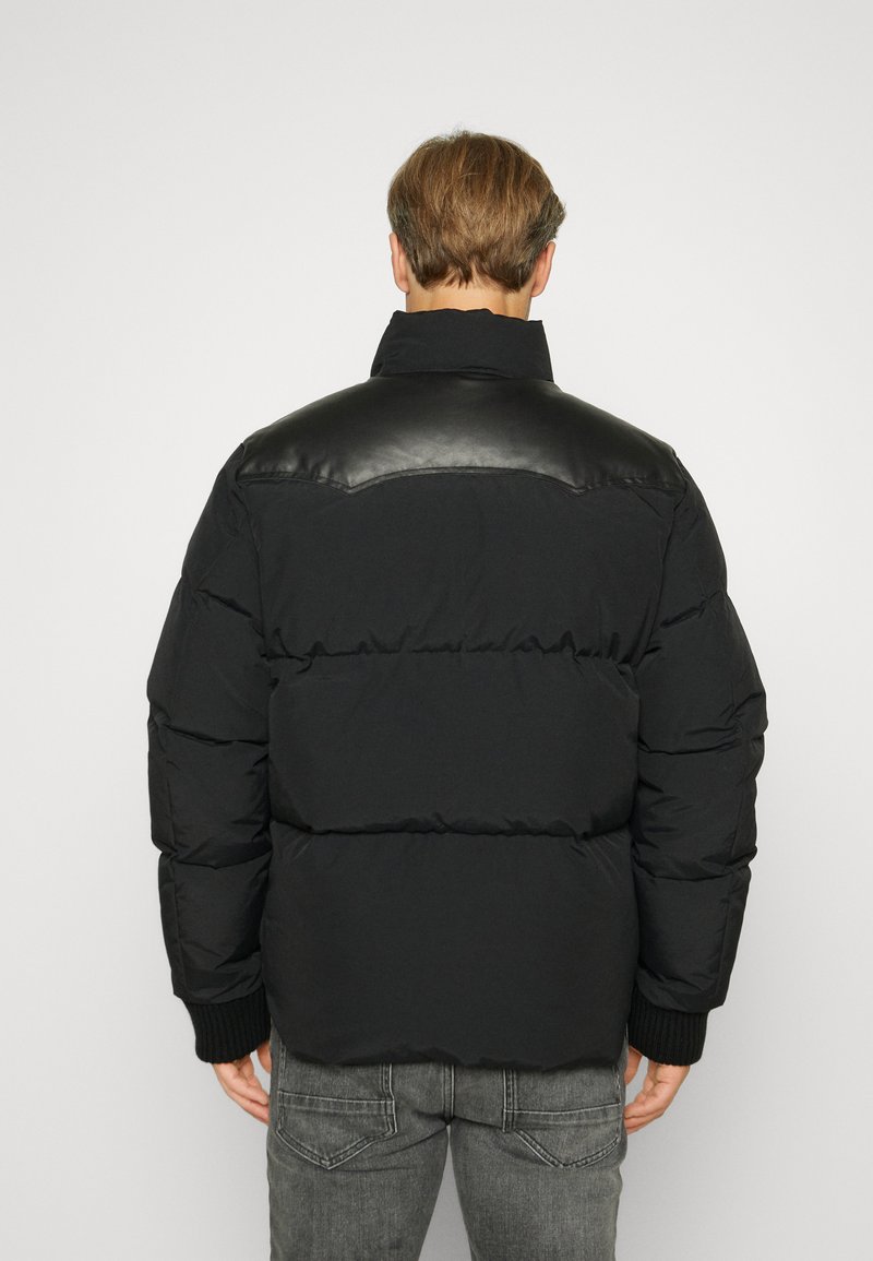 Giubbotto imbottito nero con spalla in pelle, polsini a costine e colletto alto. Presenta un design trapuntato e imbottito per garantire calore.