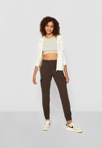 Bruna cargobyxor med avsmalnande benslut, tillverkade av bomull. Kombineras med en ljusbeige crop-top och en vit hoodie, och kompletteras av beige sneakers.