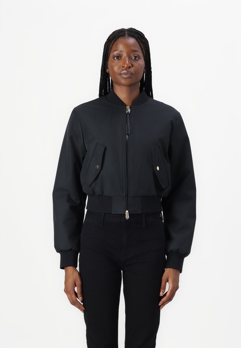 Geknipte zwarte bomberjack met een rits aan de voorkant, twee voorkruiszakken en ribgebreide manchetten. Gemaakt van een soepele stof met een matte afwerking.