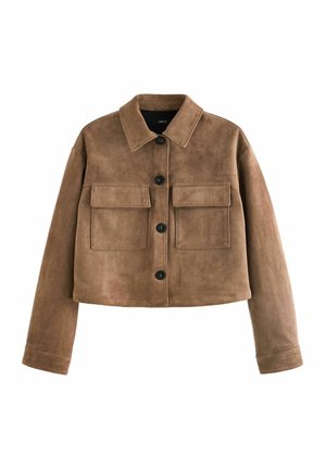 Femme portant une veste courte en daim beige et un jean bleu, tenant un sac à main en cuir marron, debout dans une rue de la ville avec des bâtiments et des voitures flous.