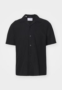 Czarna lniana koszula z krótkim rękawem, z kołnierzykiem typu camp i guzikami z przodu, wyeksponowana na jednolitym jasnym tle.