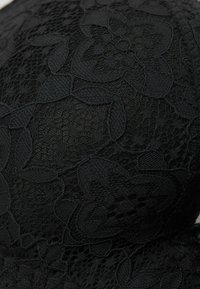 Černý krajkový bralet s květinovými vzory, texturovanou tkaninou, hladkými okraji a bezproblémovým designem. Žádné viditelné kovové části nebo ozdoby.