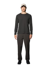 Langærmet grå top med rund halsudskæring, parret med mørke bukser med en sidelomme. Model bærer en beige kasket og sorte sko.
