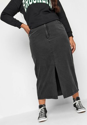 Person trägt ein schwarzes "Brooklyn"-Sweatshirt, einen taillenhohen, mittellangen Rock aus dunkelgrauem Denim mit Frontschlitz und schwarze High-Top-Sneaker mit weißen Schnürsenkeln.