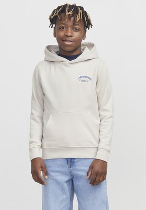Sweat-shirt beige avec poche kangourou, capuche ajustable et logo bleu sur la poitrine. Associé à un jean en denim bleu clair.