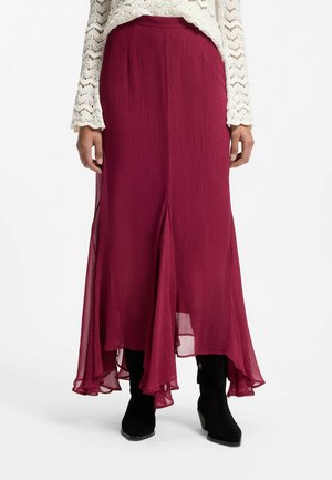 Mujer con una falda fluida de color rosa oscuro con un dobladillo irregular, combinada con botas negras y un top blanco de punto de manga larga.