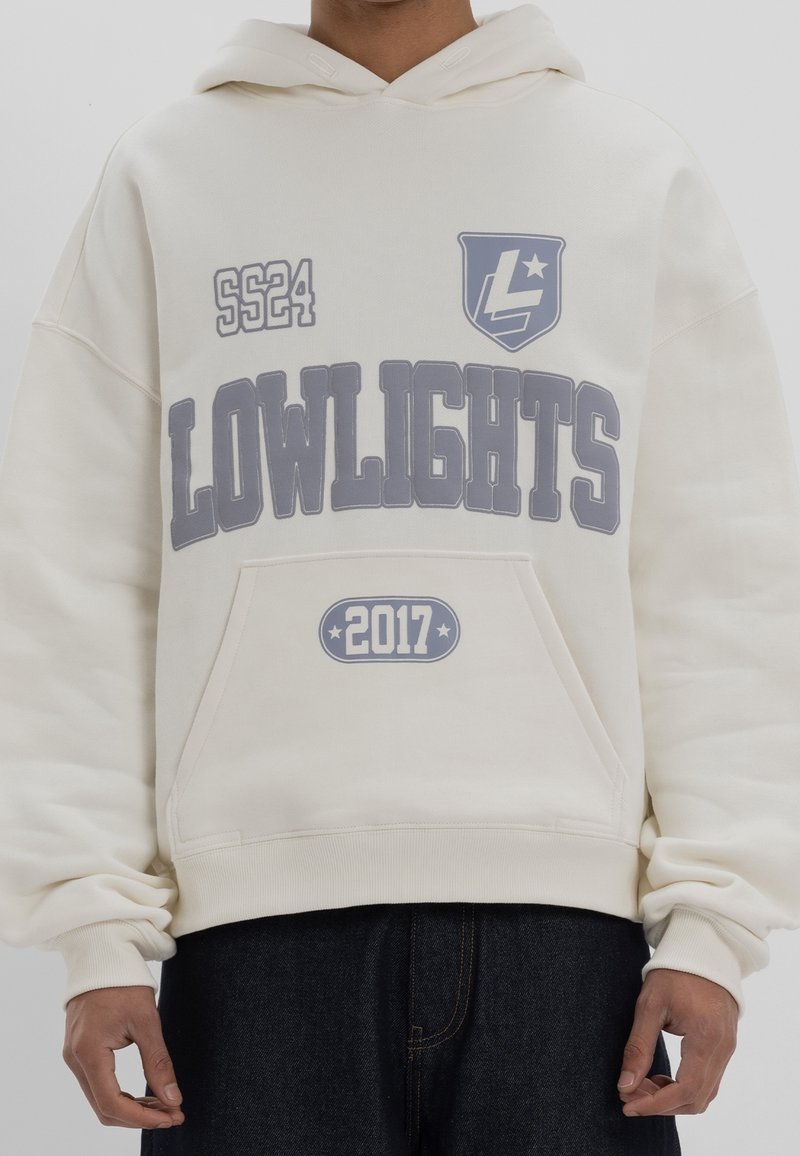 Sweat à capuche couleur crème avec un grand graphisme gris "LOWLIGHTS" accompagné des textes "2017" et "SS24". Comprend une poche kangourou et une capuche ajustable.