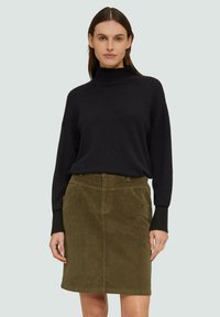 Czarny dzianinowy sweter z golfem, zestawiony z zieloną mini spódnicą z korduroju, która ma kieszenie z przodu i klasyczny krój.