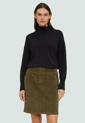 Un pull à col roulé noir en tricot associé à une mini-jupe en velours côtelé verte avec des poches avant et une coupe classique.