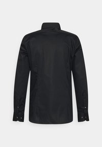 Chemise noire à manches longues avec un col classique, fabriquée en tissu doux. Présente des poignets boutonnés et un design minimaliste au dos.