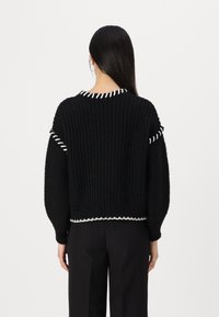 Svart strikket genser med hvite detaljer. Har ribbet tekstur, rund halsutskjæring og en cropped passform. Lange, puffete ermer.