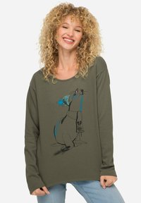 Olivegrünes Langarmshirt mit einem verspielten Grafikdesign eines Hundes, der einen blauen Hut trägt und eine Pflanze hält, aus weichem Stoff gefertigt.