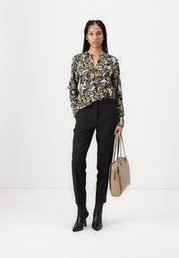 Langermet svart og gul blomstret bluse med V-hals, kombinert med svarte tapered bukser. Bærer en lys brun håndveske; bruker svarte ankelstøvler.