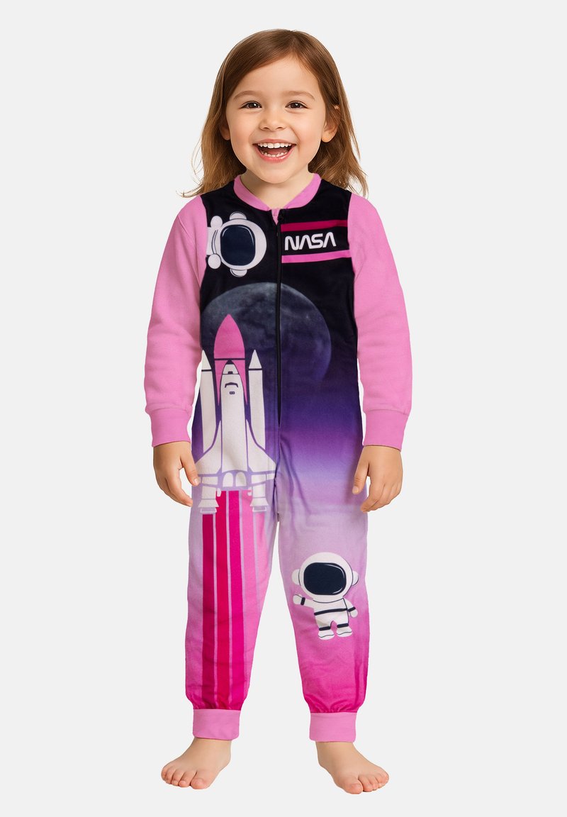 Bambino sorridente che indossa pigiami a tema NASA rosa e viola con grafiche di navette spaziali, astronauti e lune, in piedi scalzo su uno sfondo bianco.