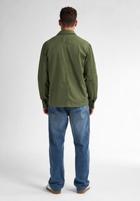 Green cotton shirt with a back yoke and buttoned cuffs, paired with blue denim jeans. The outfit features a relaxed fit and simple design.