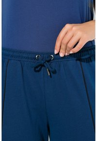 Navyblaue Jogginghosen mit einem elastischen Bund und Kordelzug. Der Stoff ist glatt mit schwarzen Akzentstreifen an den Seiten.